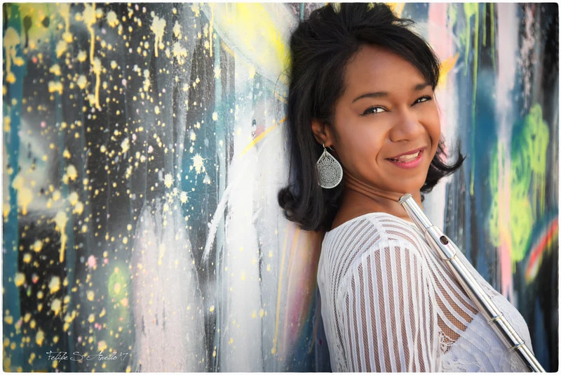 Magela Herrera smiling against a painted graffiti wall, holding her flute