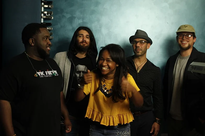 Magela Herrera laughing with four fellow musicians against a teal wall