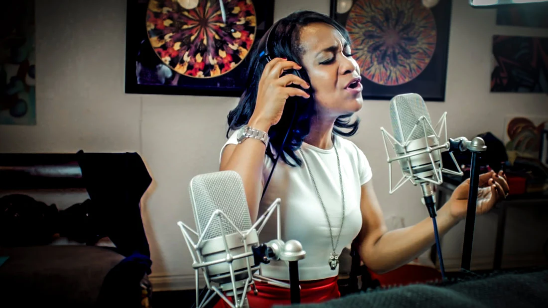 Magela Herrera singing into a studio microphone while wearing headphones