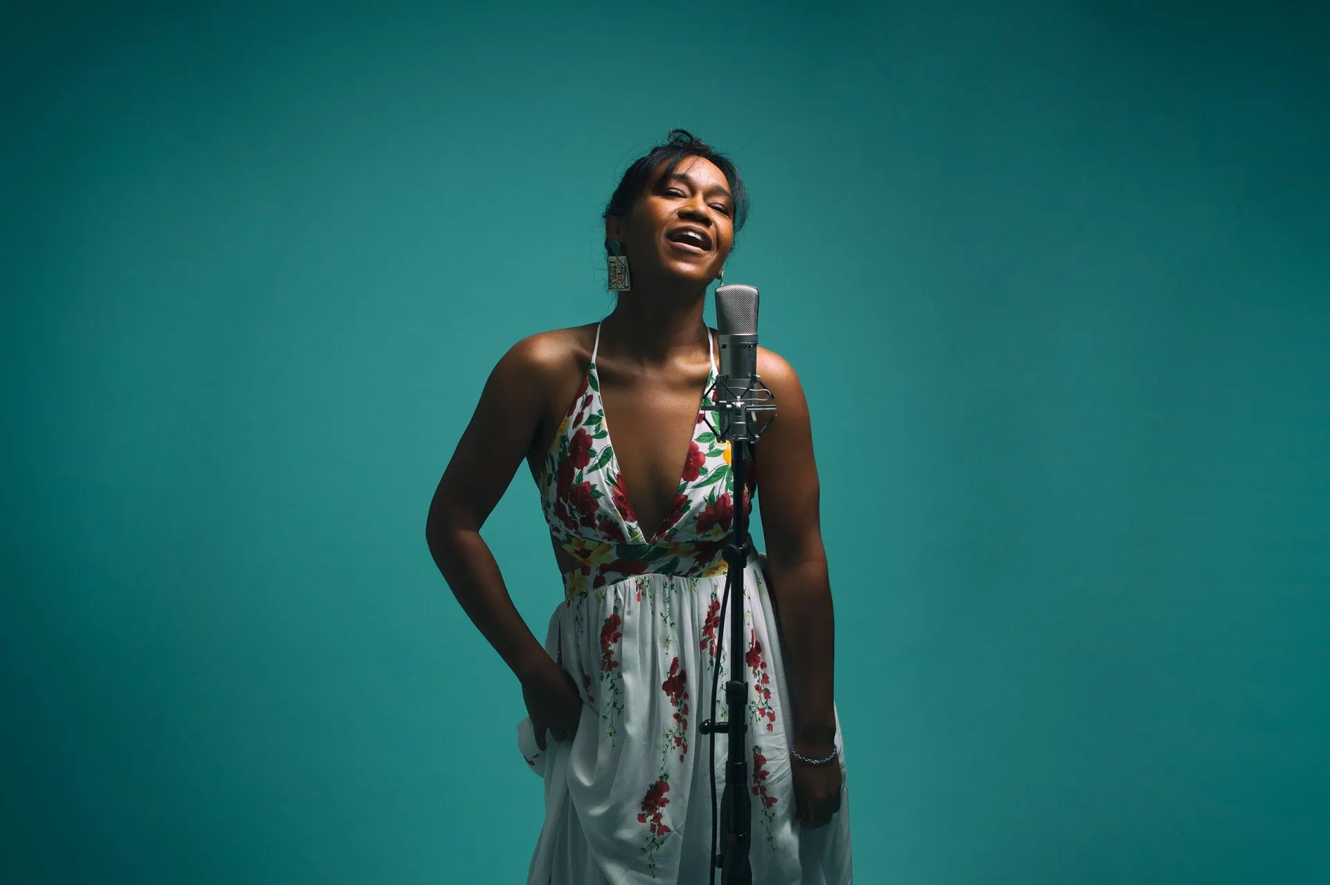Magela Herrera singing at a microphone against a teal backdrop