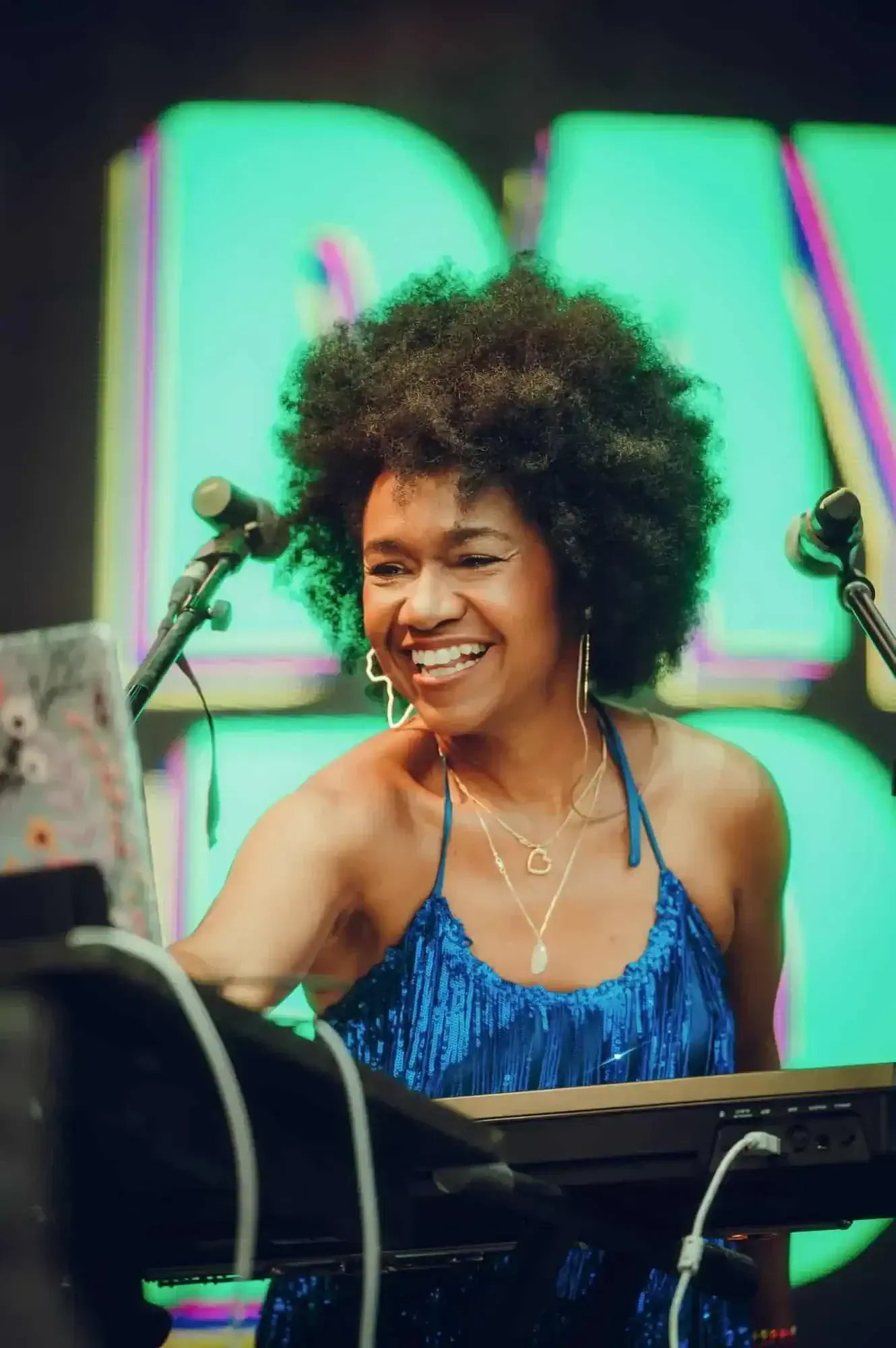 Magela Herrera smiling at the keyboard in a blue sequined dress before a green screen
